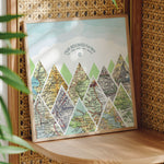 Mountain scape relief with inset maps in a square. Geometric clouds above. Sitting on shelf in thin wood frame.