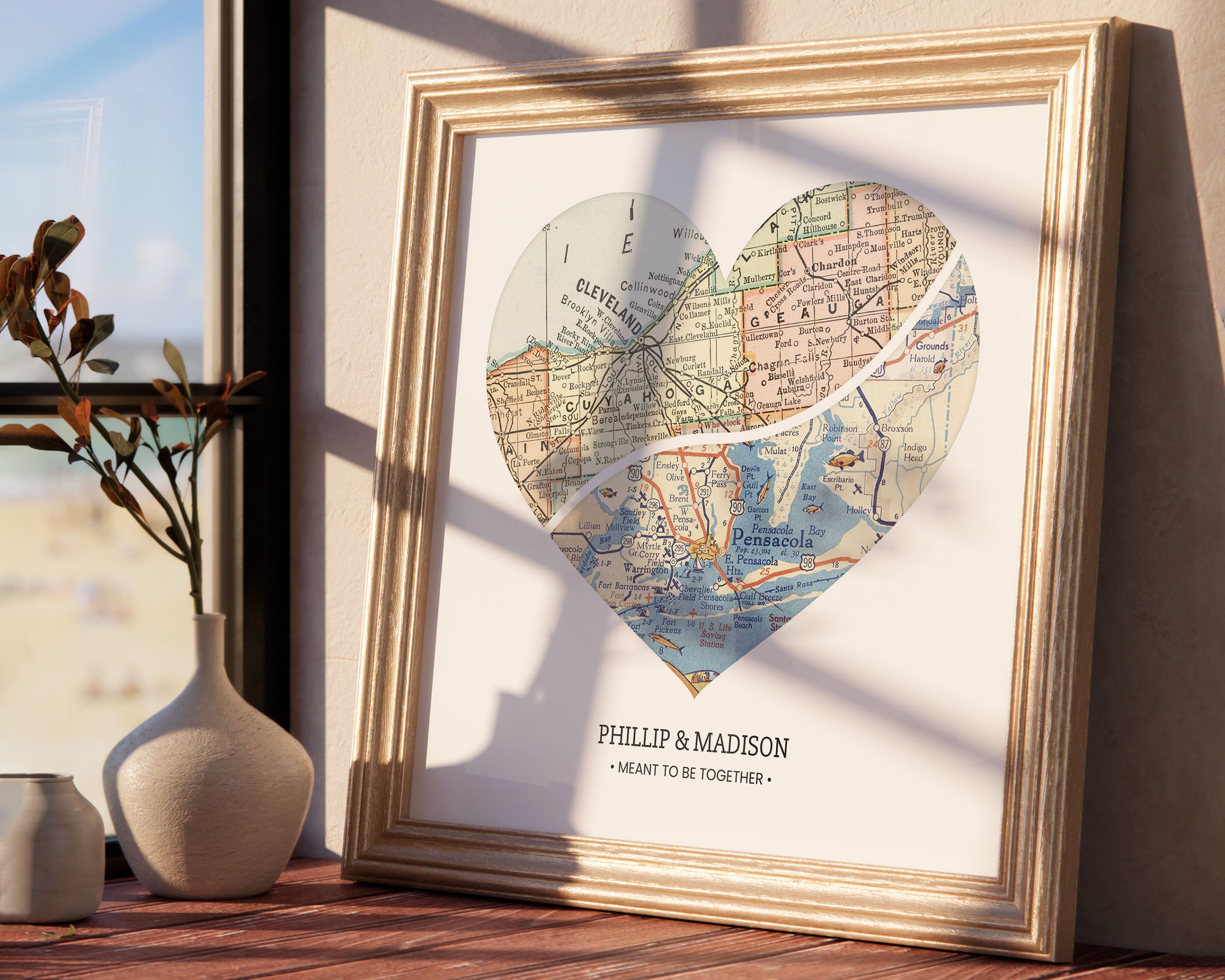 A framed heart-shaped map print with custom text, displayed on a table next to a vase with dried plants, providing a sentimental decoration reminiscent of special places and people.