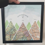 [Black Frame|12x12|3 Maps] Mountain scape relief with inset maps and geometric clouds above. Hand holding frame