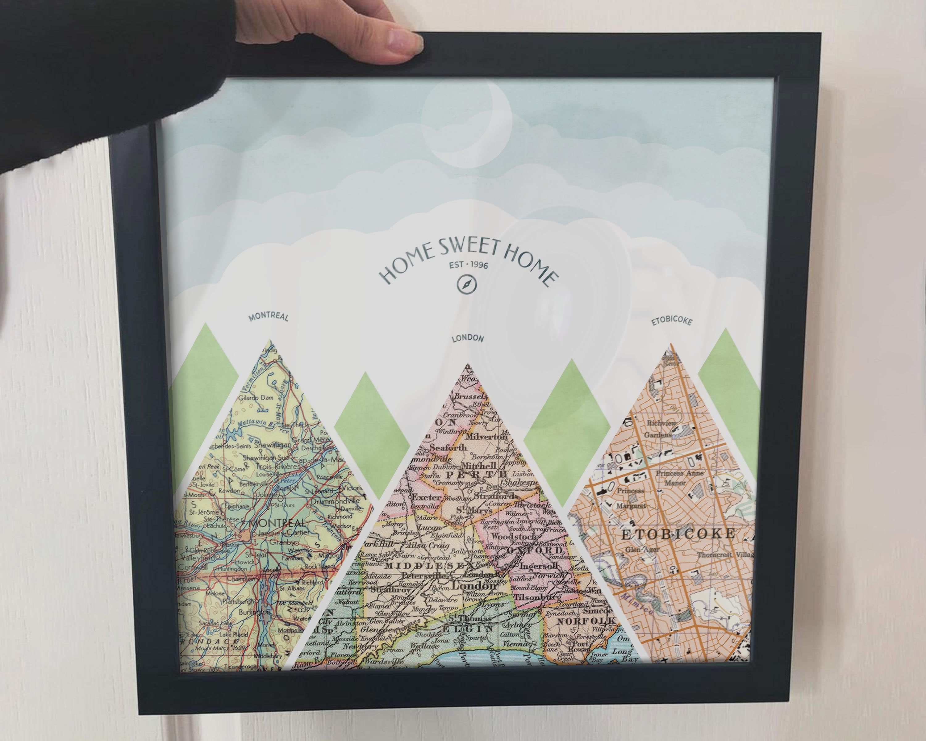 [Black Frame|12x12|3 Maps] Mountain scape relief with inset maps and geometric clouds above. Hand holding frame